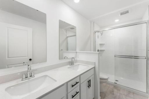 A dual-sink vanity with separate plate-glass mirrors and a glass-enclosed shower promote timely routines
