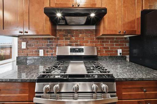 A five burner gas range set against a brick backdrop. This is where Sunday sauce simmers for hours and nobody minds the wait.