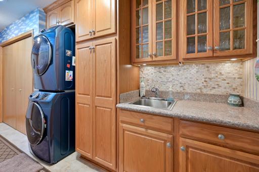 Main floor laundry room off garage with newer stackable washer and dryer with custom cabinets surrounding sink and beautiful backsplash.