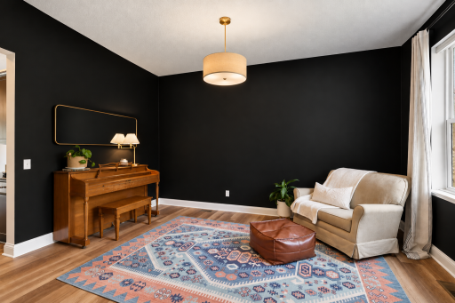 A versatile main-level flex room features dramatic black walls, warm wood-look flooring, and abundant natural light from a large window. Ideal for a home office, music room, reading lounge, or additional sitting area.
