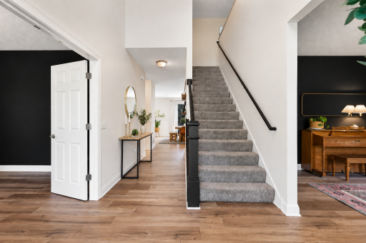 A welcoming entryway features warm wood-look flooring, a carpeted staircase, and crisp black accent walls that add a modern touch. Open sightlines into the adjoining living spaces create an inviting, connected main-level layout.
