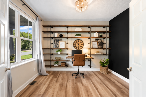 Versatile main-level office or flex space featuring stylish built-in shelving, warm wood flooring, a bold black accent wall, and abundant natural light.
