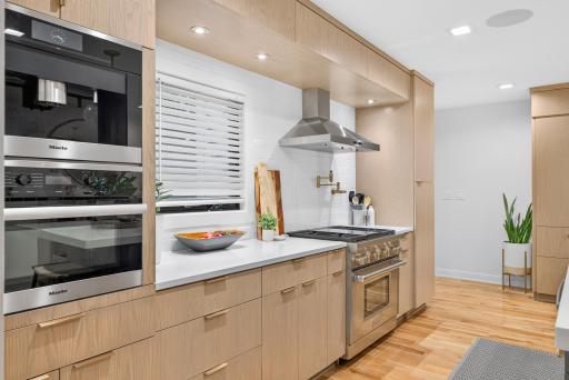 Cooking area with natural wood cabinetry, subway tiled backsplash, Miele espresso maker and convection microwave, Wolfe stainless range and pot filler.