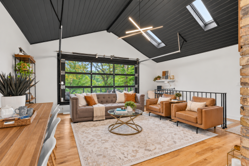 Spacious main floor living room with vaulted paneled ceiling, skylights, hardwood floors and contemporary lighting. Full-view glass garage door opens directly to the outdoor living space.