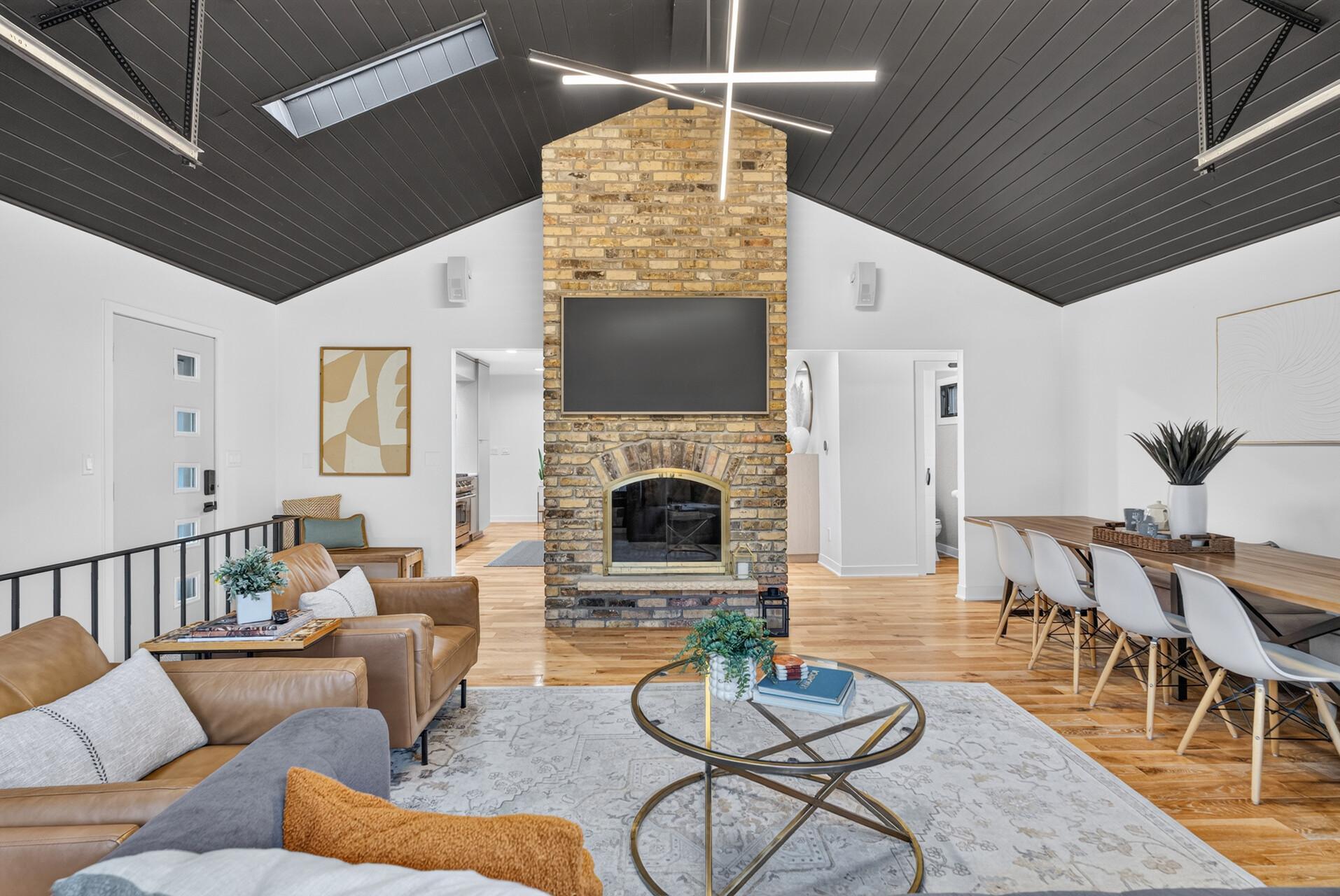 Floor-to-ceiling brick fireplace anchors the space, complemented by the dramatic vaulted ceiling, skylights and modern lighting.