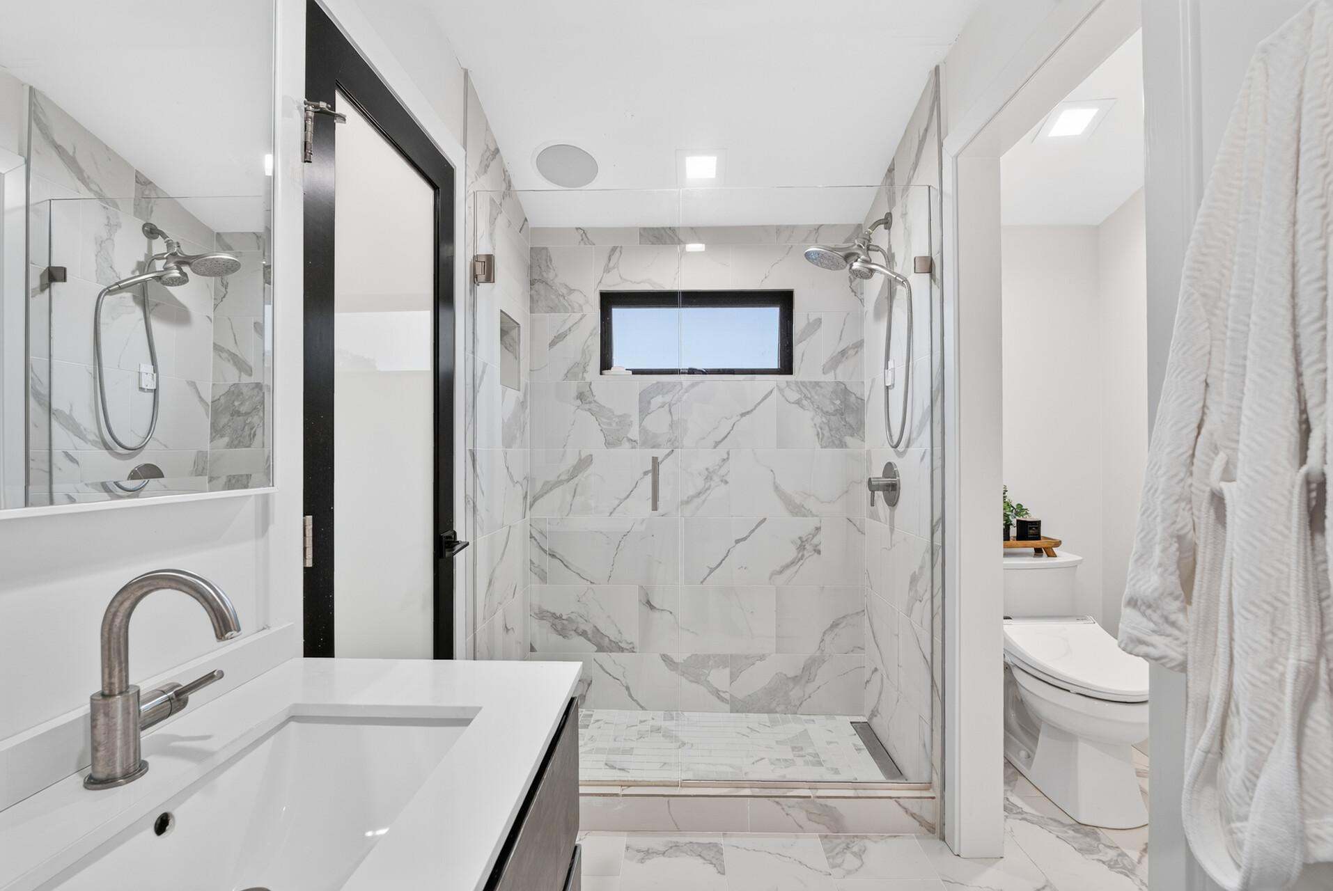 Large walk-in shower with floor-to-ceiling tile, frameless glass enclosure, built-in niche and window for natural light.