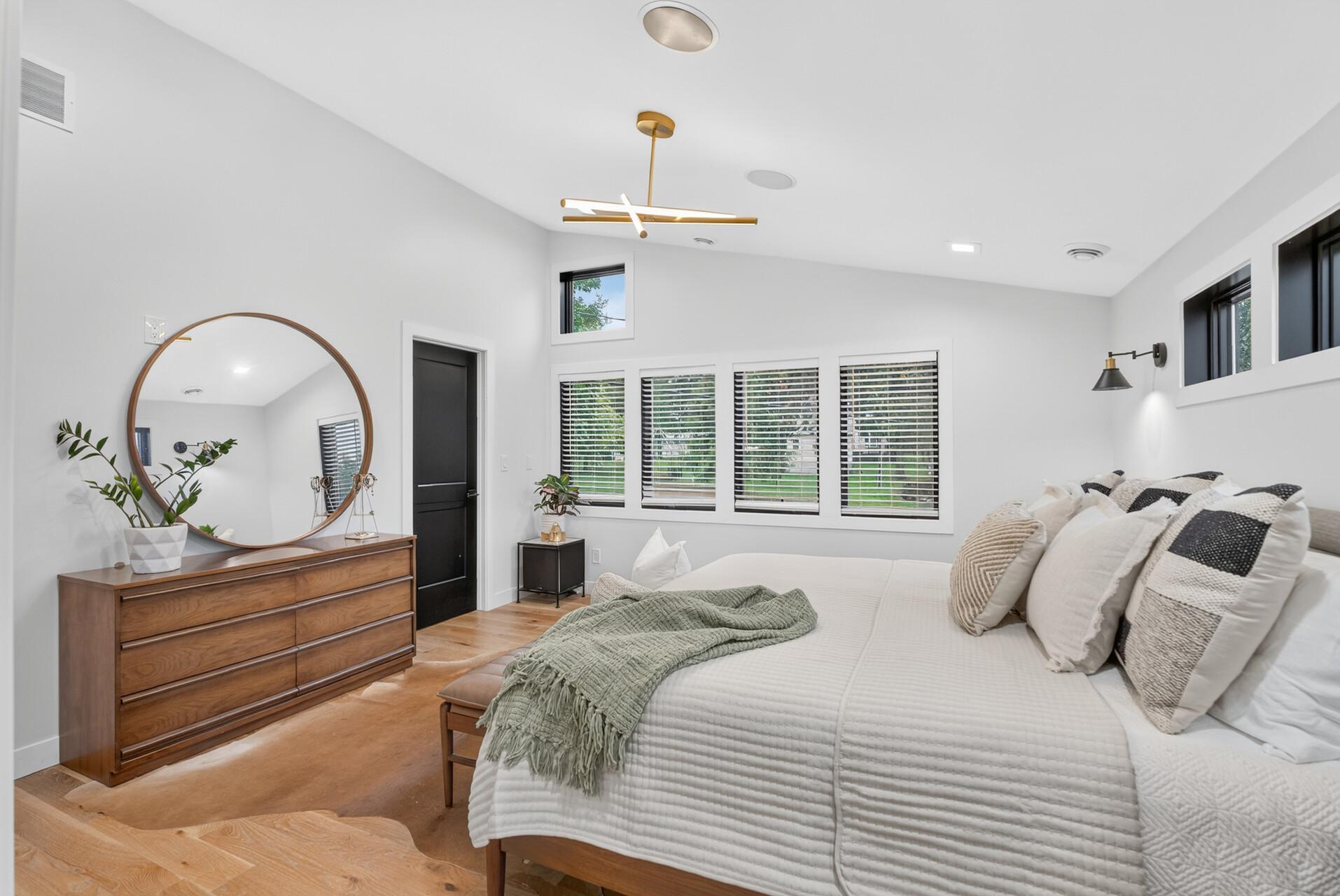 Spacious primary bedroom with vaulted ceiling, hardwood floors, multiple windows and contemporary lighting