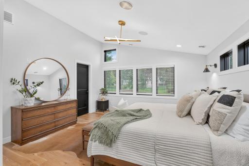 Spacious primary bedroom with vaulted ceiling, hardwood floors, multiple windows and contemporary lighting