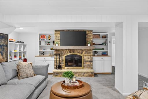Lower-level family room featuring a brick fireplace with TV above, custom built-in shelving and cabinetry, and plenty of space for comfortable seating.
