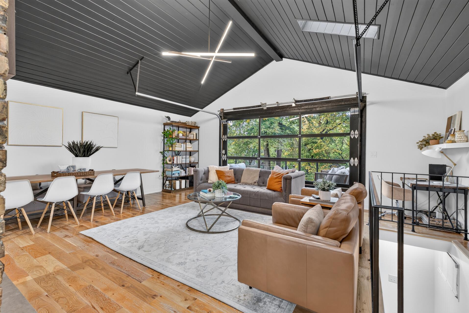 Another view of the open living room highlighting the vaulted ceiling, hardwood floors, dining area and glass garage door overlooking the backyard and access to the lower level.
