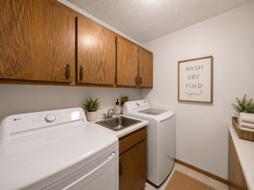 The dedicated in-unit laundry space features tile flooring, an LG washer and dryer, a utility sink, and generous cabinetry for storage and organization.