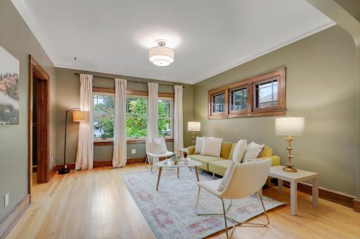 Light-filled living room showcasing hardwood floors, rich wood trim, and large windows overlooking the front yard.
