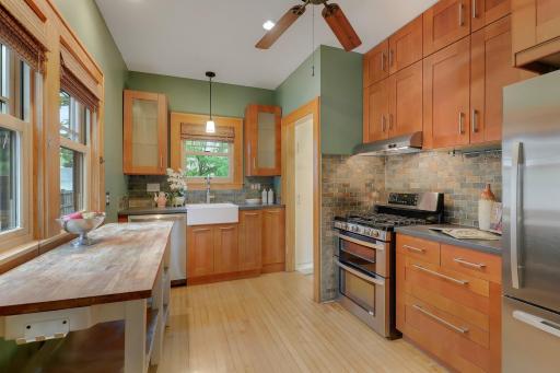 Charming kitchen featuring wood cabinetry, a farmhouse sink, stainless steel appliances, and a tiled backsplash.
