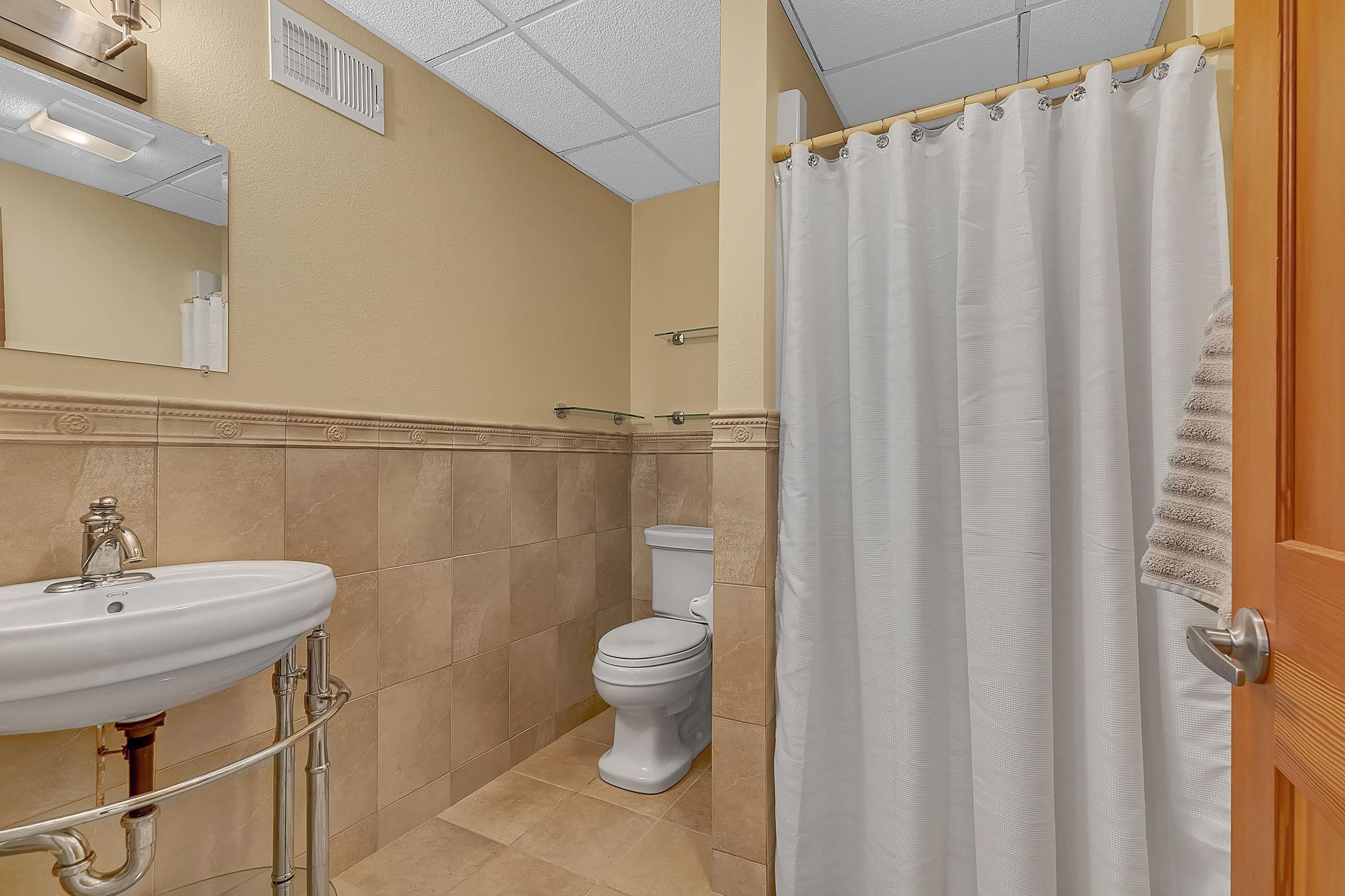 Additional 3/4 bath in the lower level featuring a walk-in shower, pedestal sink, and tiled floors and walls