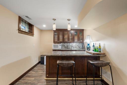 A wet bar off the recreation room features granite countertops, a sink, bar seating, and a tile backsplash, making it a great spot for entertaining.