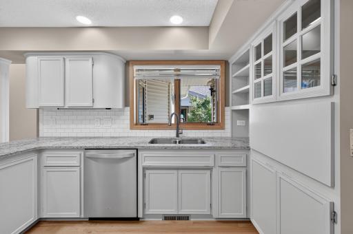 The light and bright kitchen has gorgeous quartz counters, loads of cabinets, a beautiful tile-surround backsplash, under cabinet lighting, and stainless steel appliances.