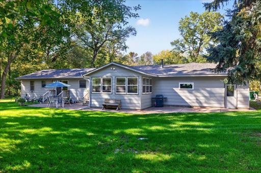 Spacious rear exterior featuring an inviting patio, enclosed porch, and beautiful views of the landscaped backyard.