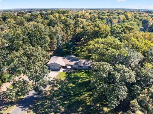 Stunning aerial view highlighting the property's approximately 1-acre setting surrounded by lush greenery and towering mature trees.
