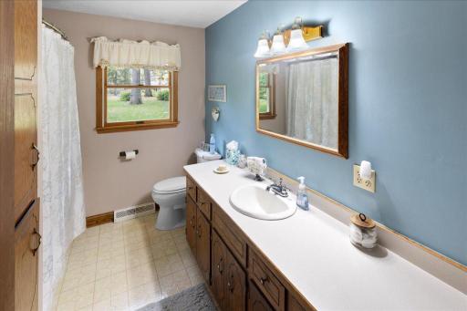 Convenient main-level full bathroom featuring a tub/shower combination, spacious vanity with ample countertop and cabinet storage, and a window overlooking the beautifully landscaped yard.