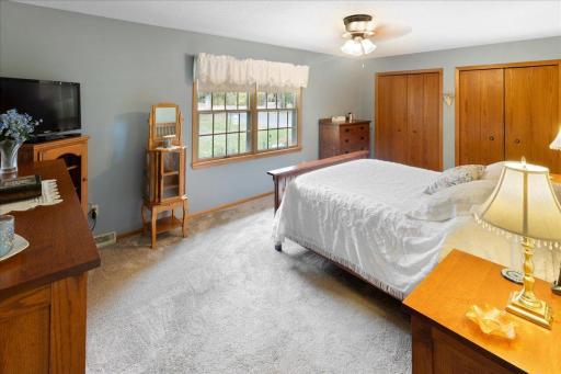 Spacious main-level bedroom featuring neutral carpeting, a ceiling fan, double windows for natural light, and generous closet space.