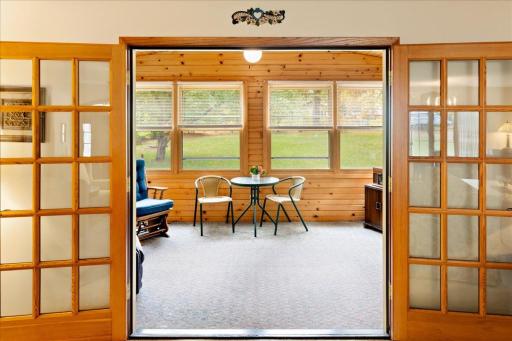 Charming enclosed porch accessed through French doors from the living room, featuring warm wood finishes and large windows overlooking the backyard.