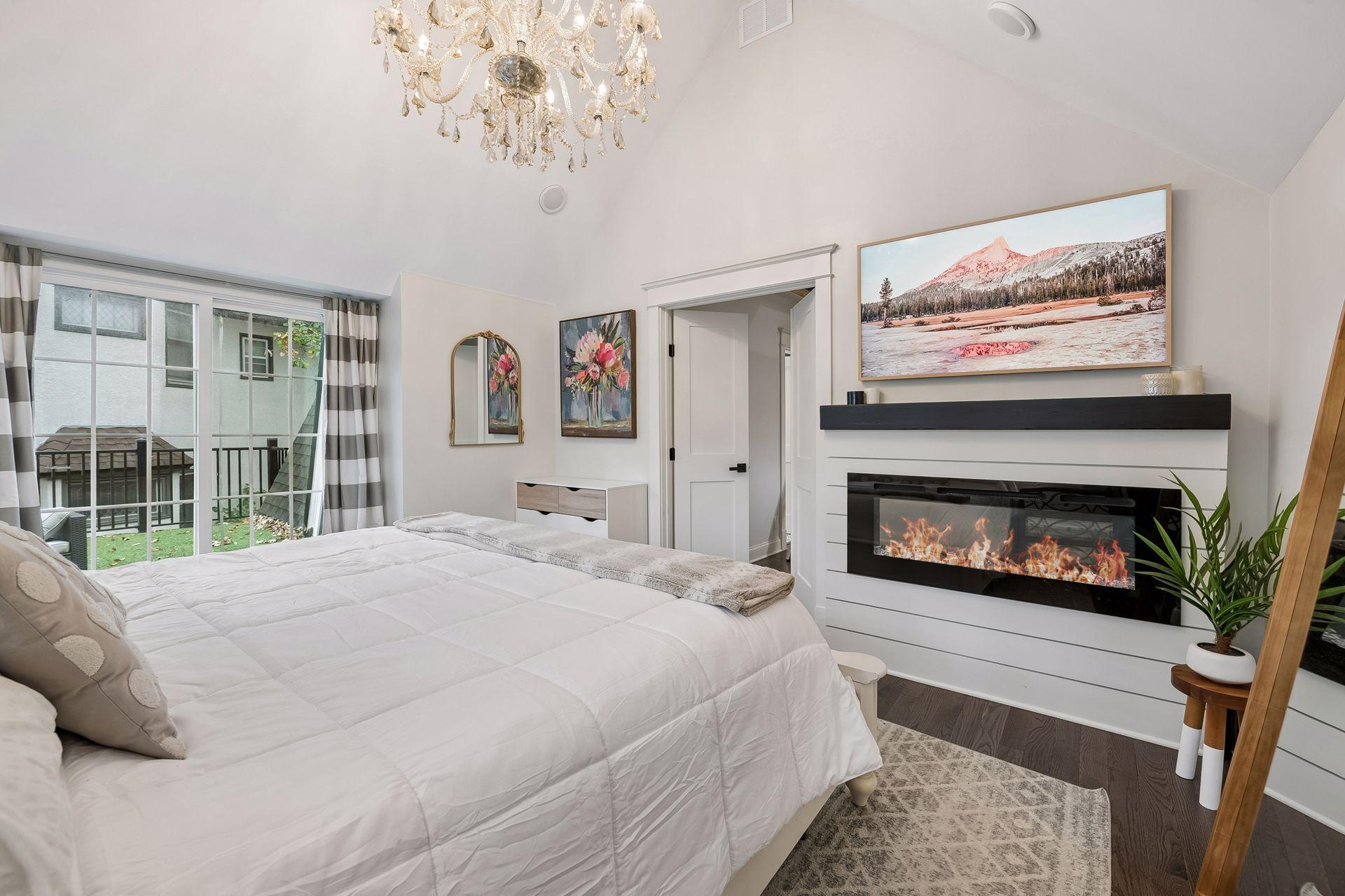 Primary bedroom includes an electric fireplace and chandelier lighting in the vaulted ceiling.