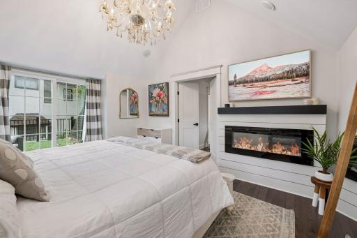 Primary bedroom includes an electric fireplace and chandelier lighting in the vaulted ceiling.