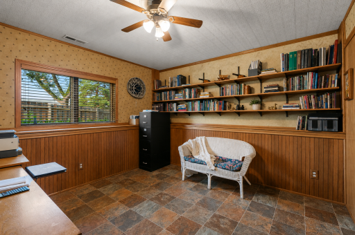 Lower-level bedroom 4, currently used as an office, is spacious with windows, custom wood paneling, built-in bookshelves, newer flooring, decorative ceiling, and a nice-sized closet