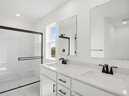 Dual quartz sinks with a full wall-width vanity mirror and a luxe glass-enclosed shower creates a spa-like atmosphere in the en-suite bathroom