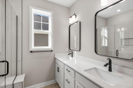 The quartz-topped vanity showcases rectangular dual sinks, stylish cabinetry and individual glass mirrors