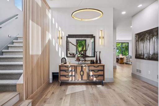 A welcoming foyer sets the tone with soaring ceilings and abundant natural light, opening to a striking staircase accented by a modern wood slat feature wall.
