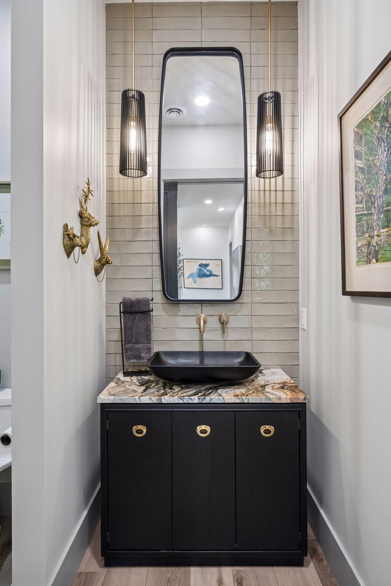 The stylish main-level half bath showcases designer finishes, featuring a custom vanity, vessel sink, statement lighting, and elegant tilework.