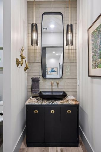 The stylish main-level half bath showcases designer finishes, featuring a custom vanity, vessel sink, statement lighting, and elegant tilework.