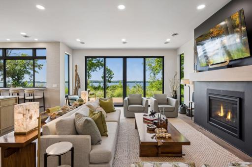 The inviting living room is anchored by a sleek fireplace and framed by expansive windows and sliding glass doors that capture stunning lake views.