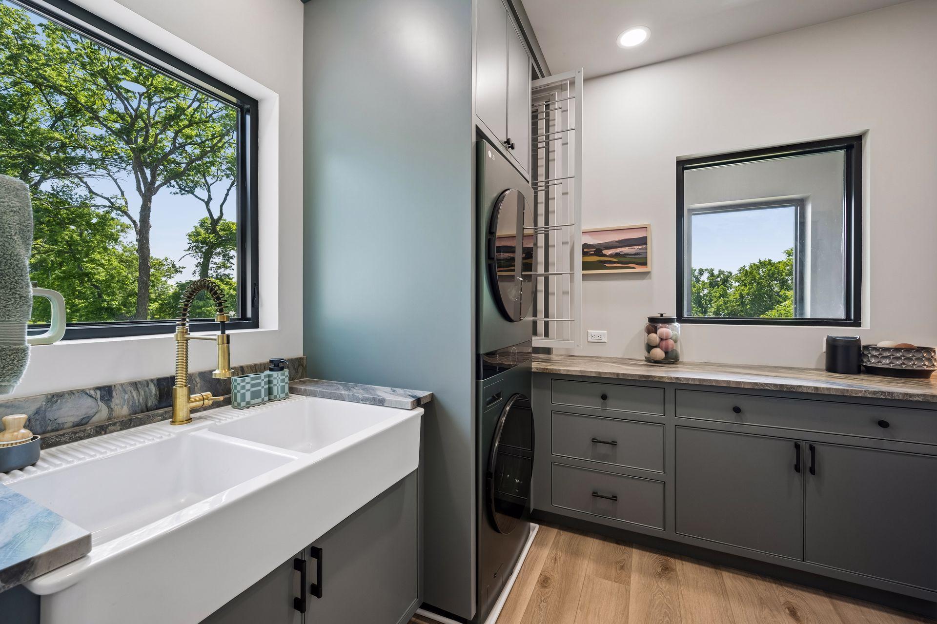 The upper-level laundry room is thoughtfully designed, featuring custom cabinetry, generous countertop workspace, a built-in drying rack, and a farmhouse sink.