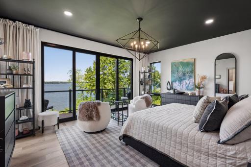 The primary suite is a private lakeside retreat, where expansive windows and sliding glass doors frame breathtaking water views and fill the room with natural light.
