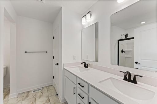 A quartz-topped vanity with dual sinks and individual mirrors optimize shared living, while a glass-enclosed shower promotes timely morning rituals