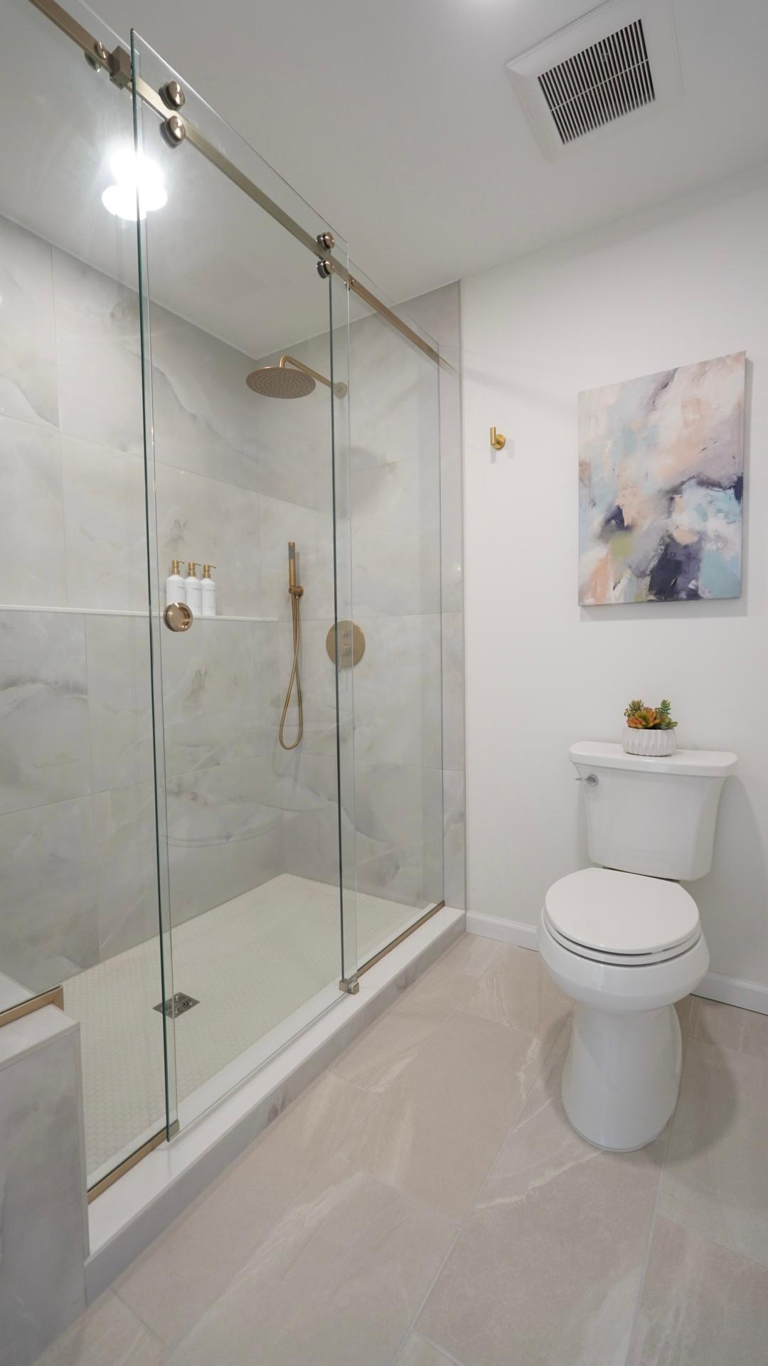 The main level private primary bathroom features a separate shower room with a massive shower with large format tile, brushed gold shower trim and a custom glass shower door.