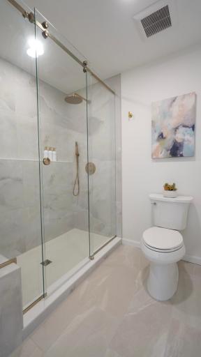 The main level private primary bathroom features a separate shower room with a massive shower with large format tile, brushed gold shower trim and a custom glass shower door.