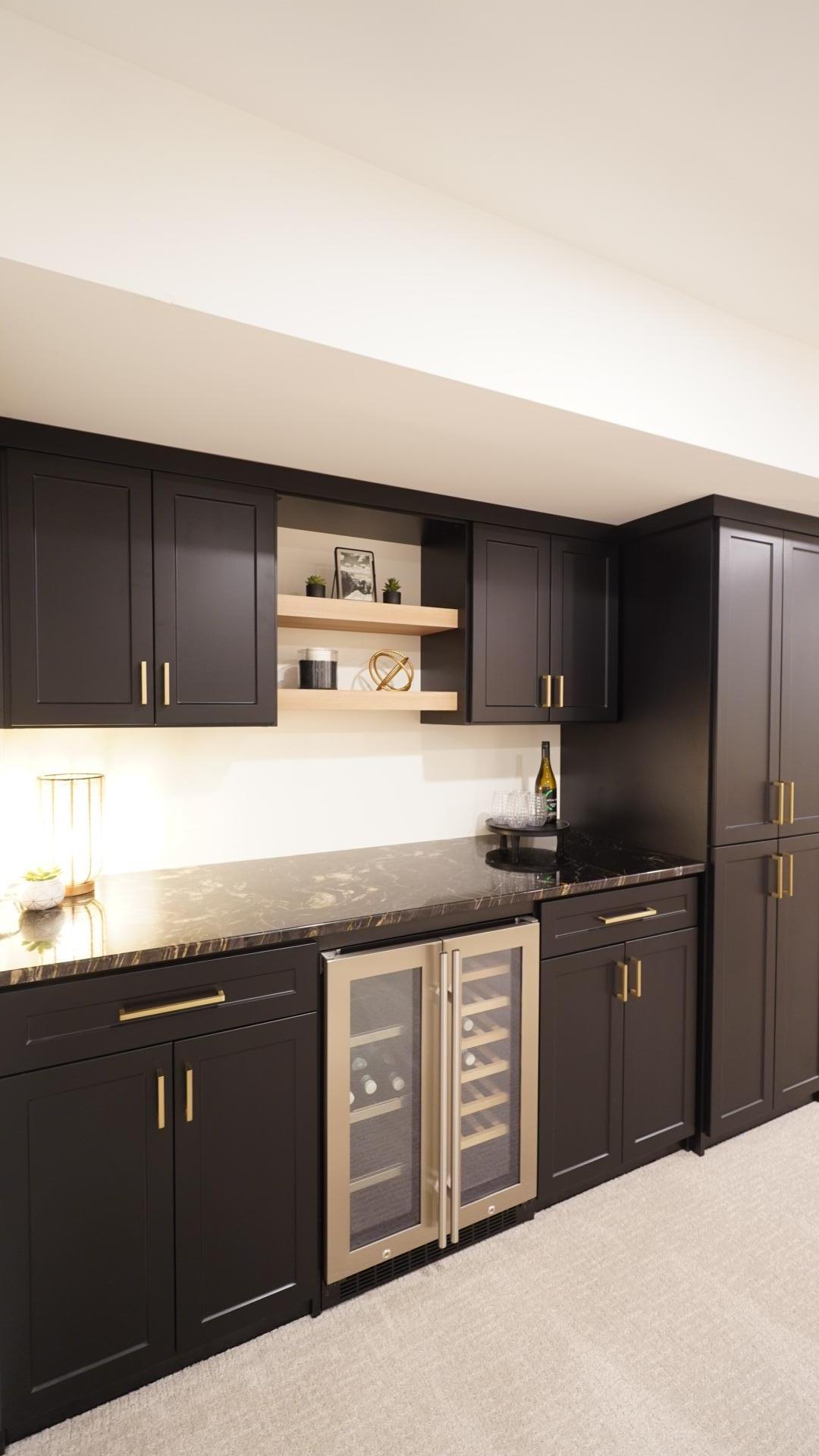 The custom dry bar is a modern and sophisticated focal point in the basement family room featuring beautiful dark granite countertops, ample storage and a built-in beverage refrigerator.