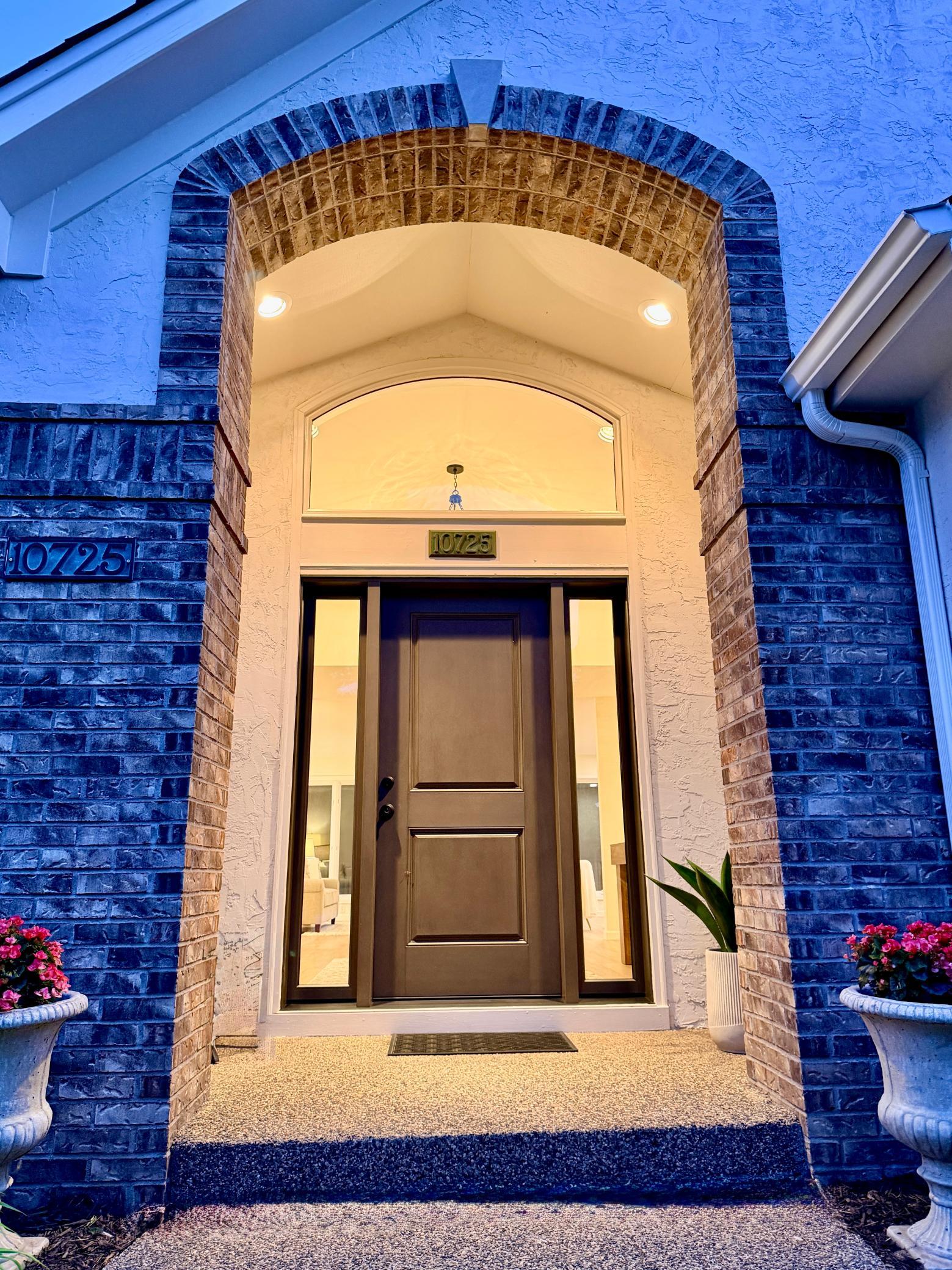 The inviting barrel vault front entry at twilight with a new front door invites you into a large foyer and an open great room that is flanked by two wings in a U-shaped floor plan.