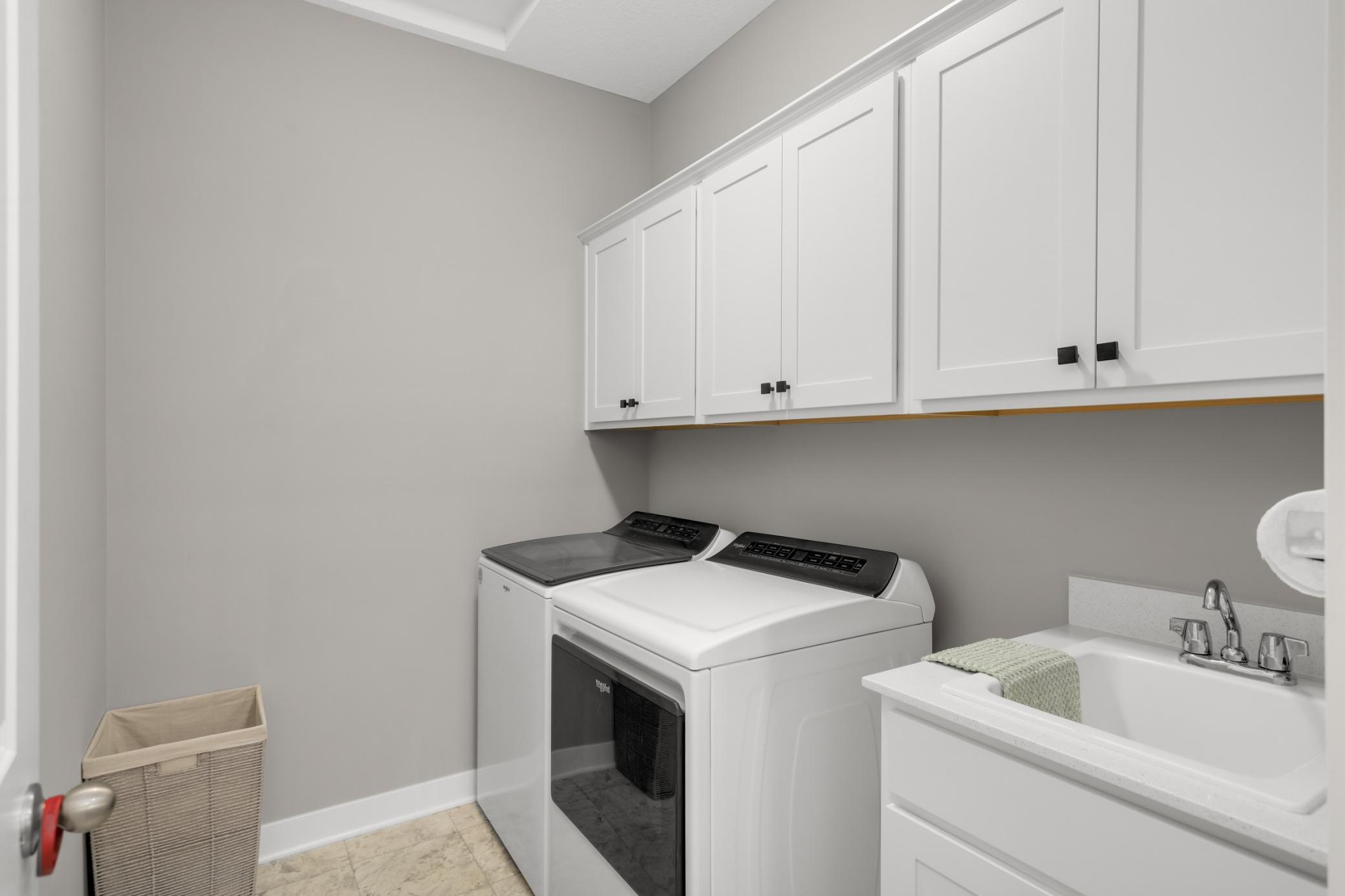 Laundry room is spacious and provides upper cabinets and a utility sink.