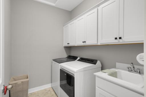 Laundry room is spacious and provides upper cabinets and a utility sink.