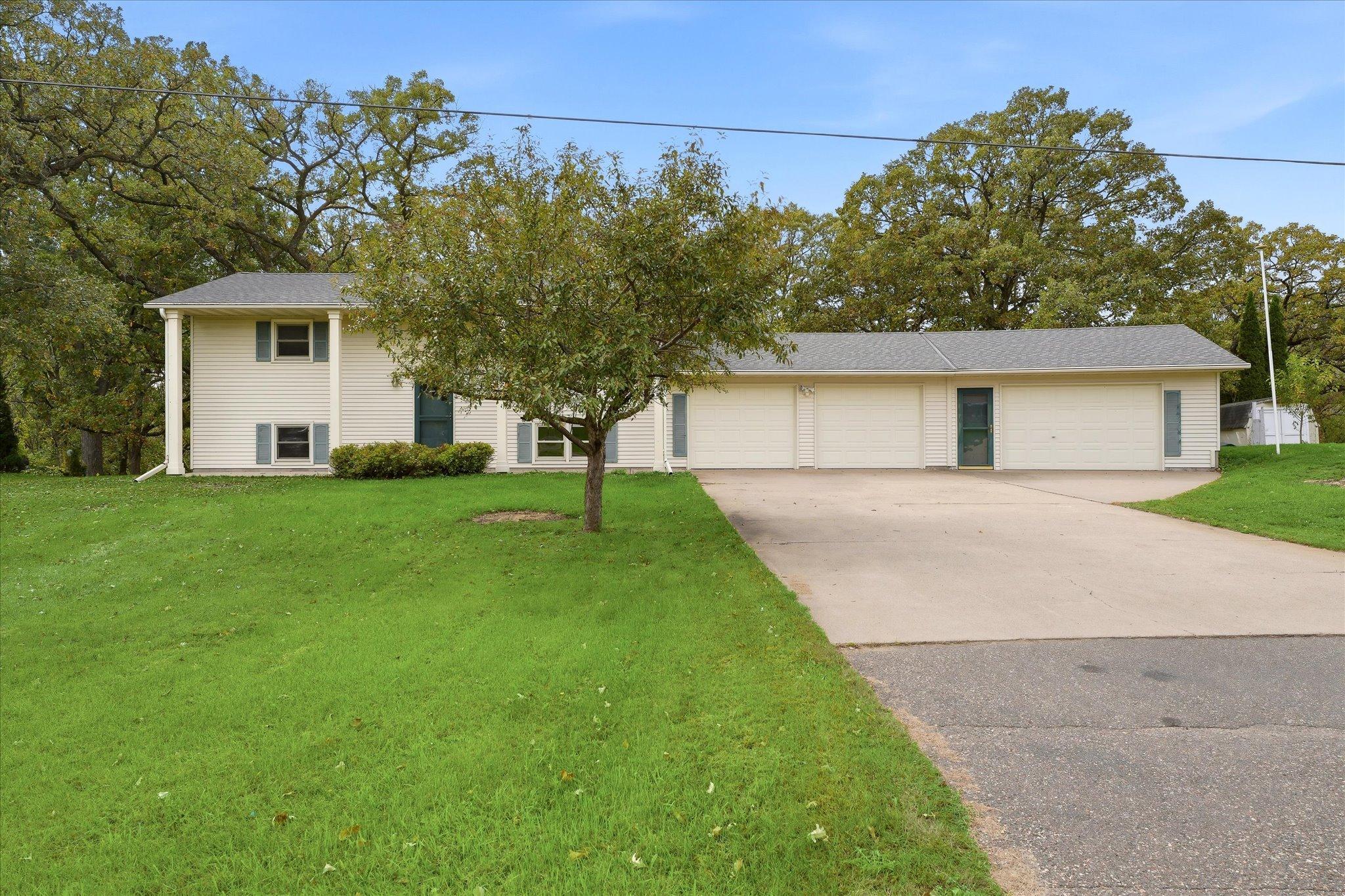 Spacious home featuring an impressive attached four-car garage (3rd and 4th stalls are heated), expansive concrete driveway, and mature trees surrounding the property.
