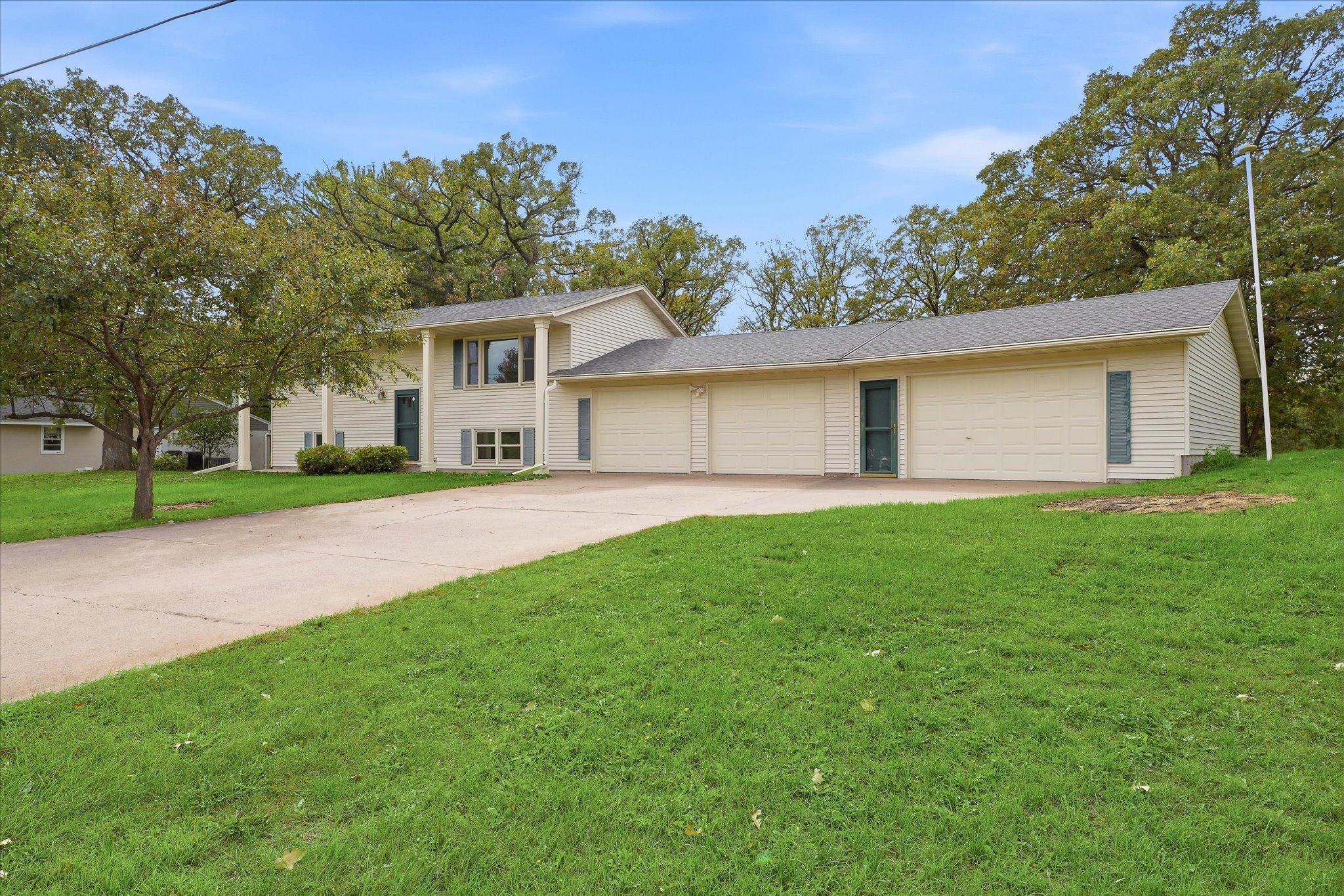 Welcoming front exterior with a large four-car garage, generous driveway, mature landscaping, and plenty of additional parking space.