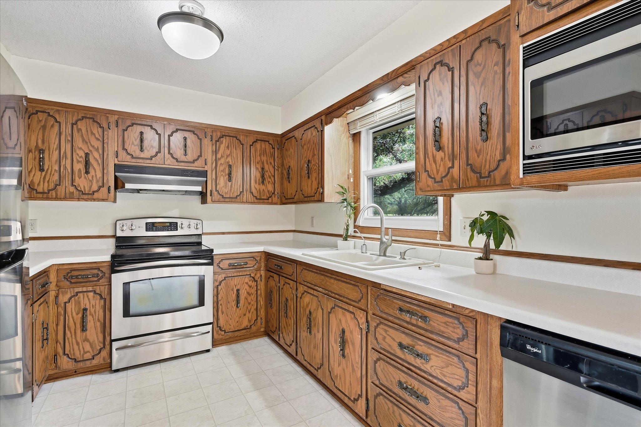 Generously sized kitchen offers an abundance of cabinetry and countertop space, stainless steel appliances, and a window above the sink overlooking the wooded backyard.