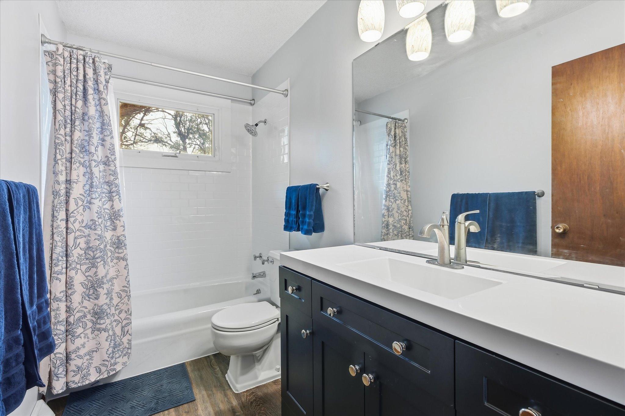Updated upper-level full bathroom features a modern vanity with generous counter space, contemporary lighting, LVP floors, and a tub/shower with classic white tile surround.