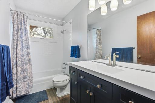 Updated upper-level full bathroom features a modern vanity with generous counter space, contemporary lighting, LVP floors, and a tub/shower with classic white tile surround.