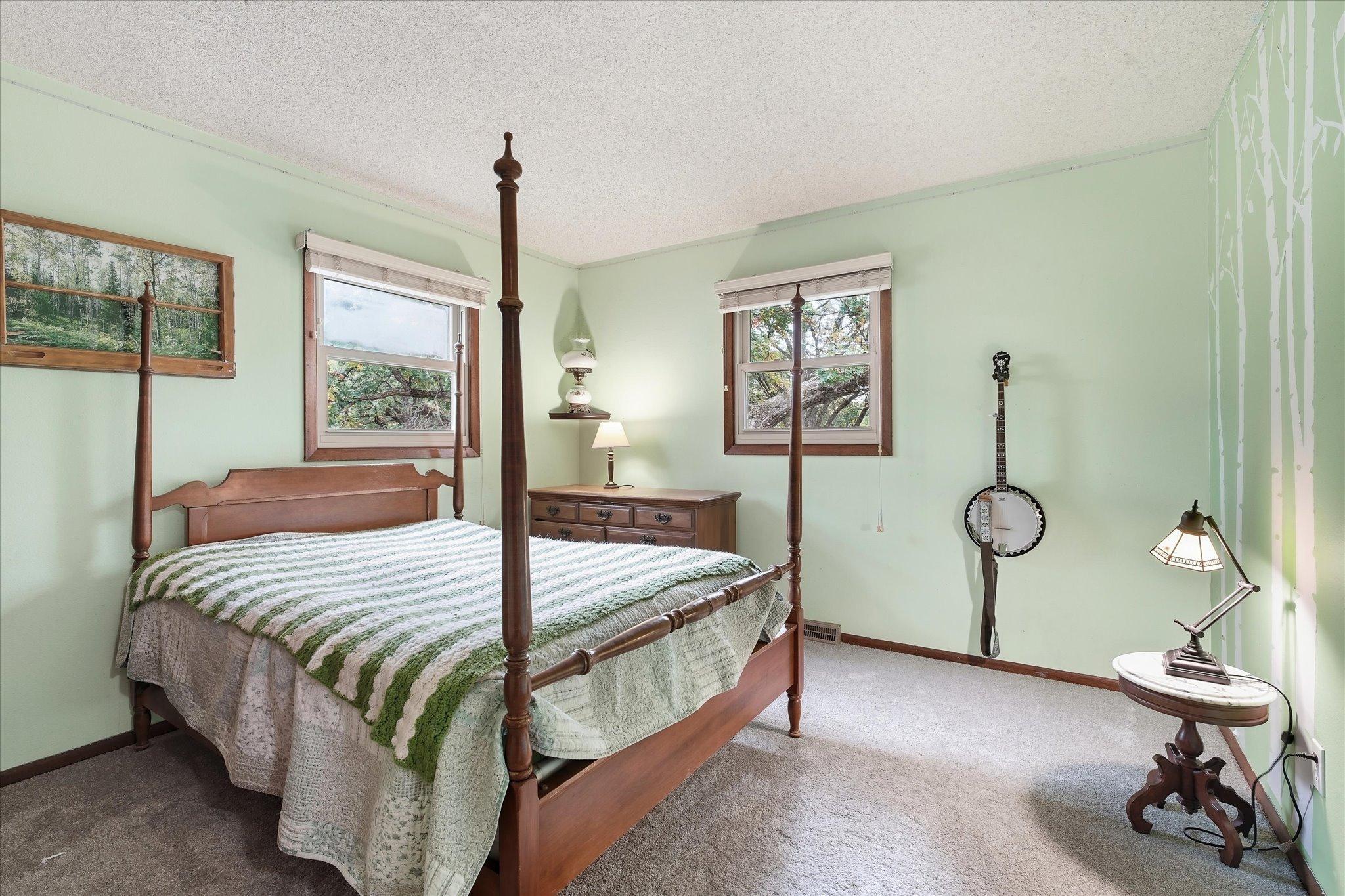Upper-level bedroom #1 offers plenty of natural light from two windows, comfortable space for bedroom furniture, and peaceful views of the surrounding trees.