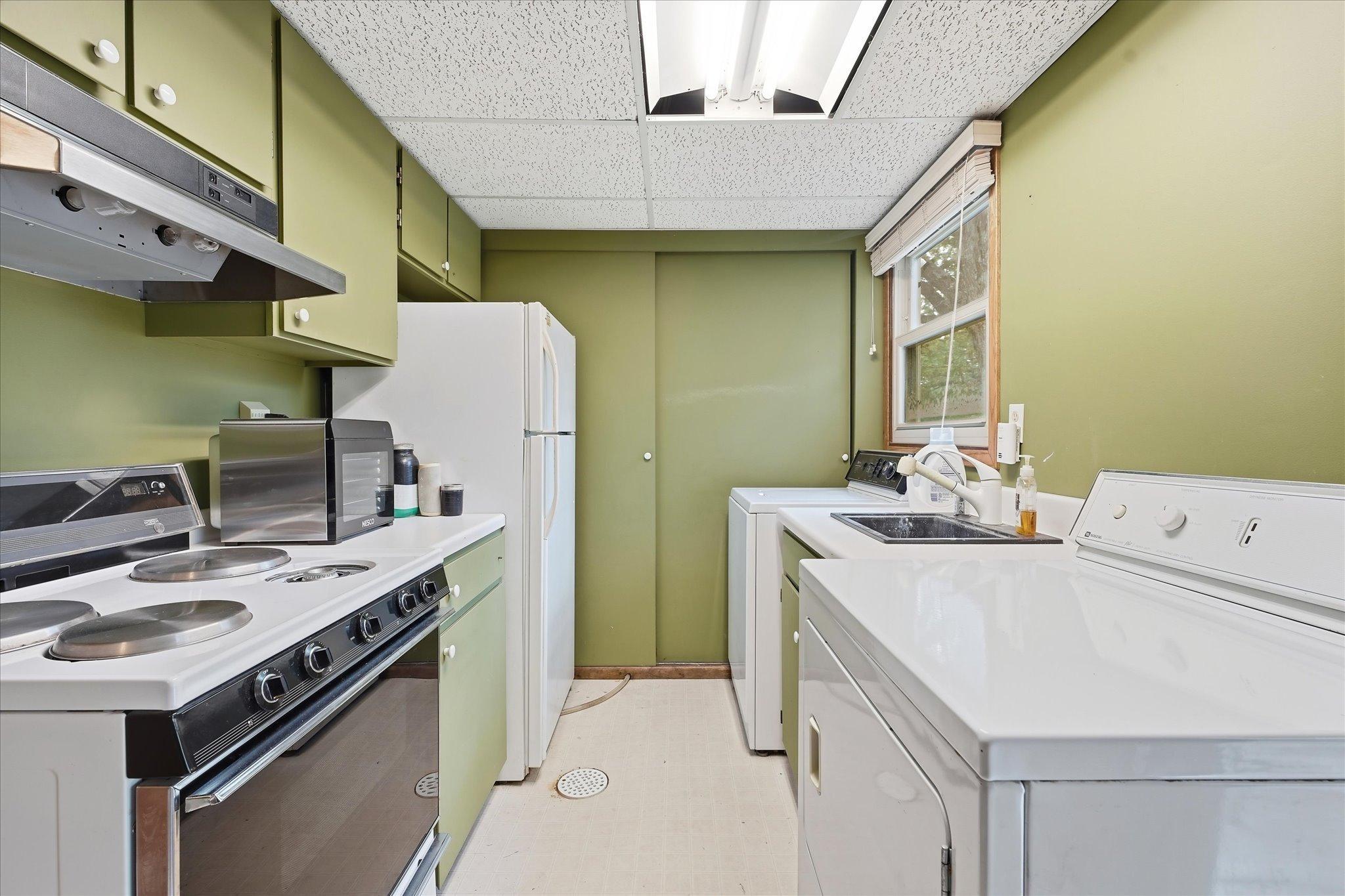 Versatile lower-level laundry room featuring a convenient second kitchen with stove, refrigerator, sink, cabinetry, and counter space.